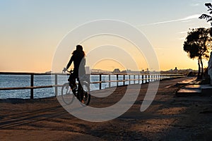 Silhouette of young curly girl riding a bicycle at the sunset on the promenade road of Maresme, Catalonia, Spain photo