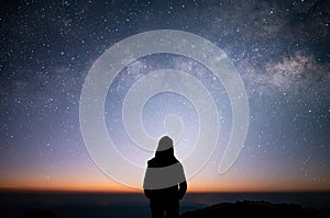 Silhouette of young female standing and watched beautiful view sunrise, star and milky way alone on top of the mountain. She