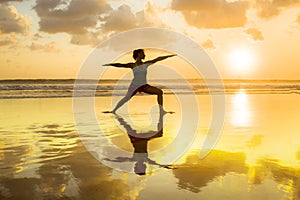 Silhouette of young fit and healthy attractive woman practicing fitness and yoga in beautiful sunset beach in meditation and relax