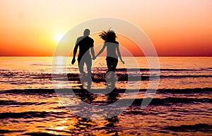 Silhouette of young fitness couple walking inside the water at sunrise - Multi race people having fun on vacation - Romantic and