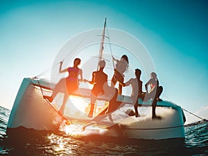 Silhouette of young friends chilling in private catamaran boat - Group of people making tour ocean trip - Alternative travel photo