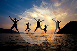 Silhouette of young friends having fun on the beach and jumping