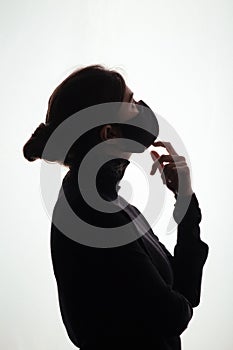 Silhouette of young frightened woman in black protective mask on studio background,criminal surrenders raising his hands, concept