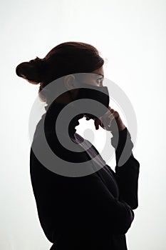 Silhouette of young frightened woman in black protective mask on studio background,criminal surrenders raising his hands, concept