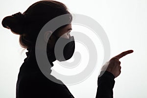 Silhouette of young frightened woman in black protective mask on studio background,criminal surrenders raising his hands, concept