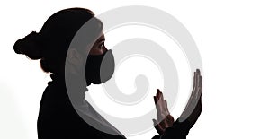 Silhouette of young frightened woman in black protective mask on studio background,criminal surrenders raising his hands, concept