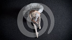 Silhouette of young girl ballerina puts on pointe, sitting on floor, ballet concept, top shot