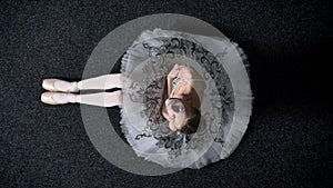 Silhouette of young girl ballerina is sitting on floor, watching up at camera, ballet concept, top shot