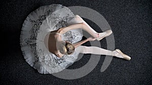 Silhouette of young girl ballerina ties ribbon on pointe, sitting on floor, ballet concept, top shot