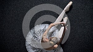 Silhouette of young girl ballerina ties ribbon on pointe, sitting on floor, ballet concept, top shot, dolly shot