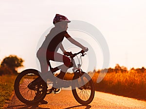 Silhouette of young girl on a bicycle at sunset