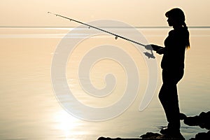 Silhouette of a young girl fishing at sunset