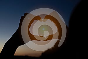 Silhouette of a young girl holding sun in her hands shaped like heart at sunset