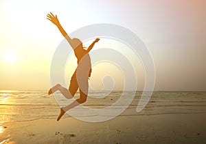 Silhouette young girl jumping with hands up on the beach