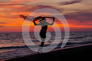 Silhouette of young girl, jumping with silk cloth against of sea sunset