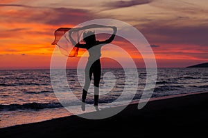 Silhouette of young girl, jumping with silk cloth against of sea sunset