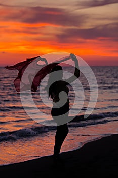 Silhouette of young girl, jumping with silk cloth against of sea sunset