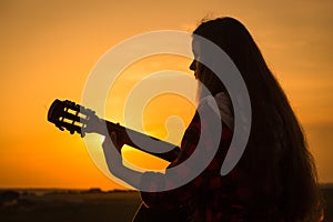 Silhouette of young girl playing the guitar at sunset