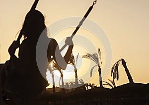 Silhouette of a young girl riding on a swing at sunset on a back