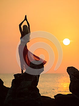 A silhouette of a young girl on rock at sunset 2