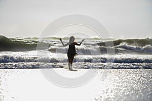 Silhouette of young happy Asian woman relaxed looking at wild sea waves on sunset tropical beach