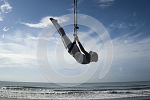Silhouette of young happy and athletic Asian Indonesian woman doing aero yoga workout training body balance hanging from swing