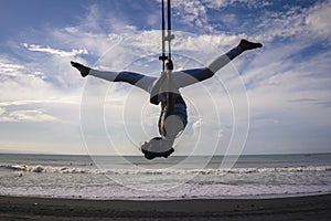 Silhouette of young happy and athletic Asian Indonesian woman doing aero yoga workout training body balance hanging from swing