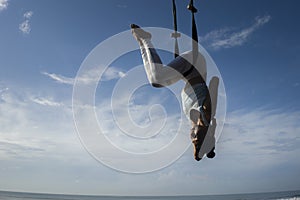 Silhouette of young happy and athletic Asian Indonesian woman doing aero yoga workout training body balance hanging from swing