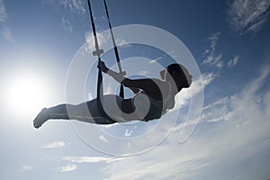 Silhouette of young happy and athletic Asian Indonesian woman doing aero yoga workout training body balance hanging from swing