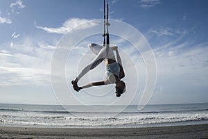 Silhouette of young happy and athletic Asian Indonesian woman doing aero yoga workout training body balance hanging from swing