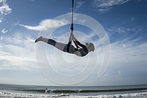 Silhouette of young happy and athletic Asian Indonesian woman doing aero yoga workout training body balance hanging from swing