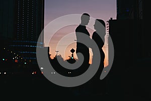 Silhouette of young happy couple in love kissing on city street at sunset