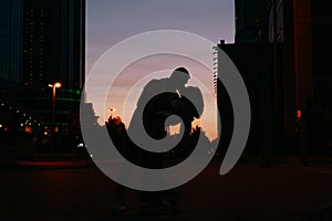 Silhouette of young happy couple in love kissing on city street at sunset