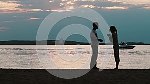 Silhouette of young happy couple talking on the beach. Man and woman walking on sunset, motorboat on the background.