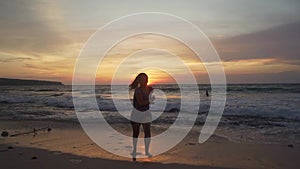 Silhouette of young happy and excited Asian woman at beautiful beach enjoying golden hour at tropical beach of Bali