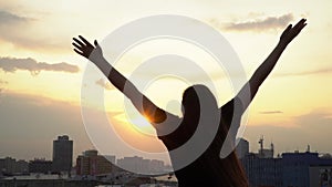 Silhouette of a young happy girl feeling awesome on the rooftop with great view over city. Success and happiness concept