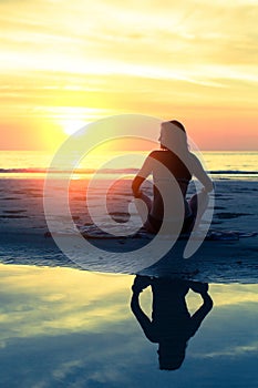 Silhouette young healthy woman practicing yoga on the beach