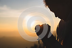 Silhouette of young  human hands praying with a  cross at sunrise, Christian Religion concept background
