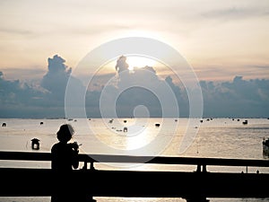 Silhouette of young lady photographer on the bridge over the sea