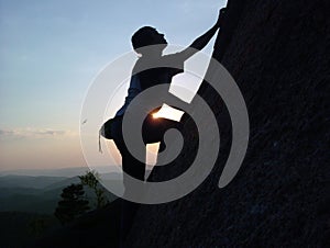 Silhouette of a young male climber climbing to the top of the cliff at sunset without insurance.