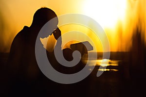 Silhouette of a young man with a Bible, male praying to God in nature, the concept of religion and spirituality