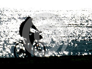 Silhouette of a young man on a bicycle riding along the seashore