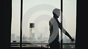 Silhouette of young man dancing ad listening music in wireles headphones stand on hotel room balcony