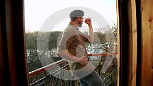 Silhouette of young man dancing ad listening music in wireles headphones stand on hotel room balcony. free lifestyle.