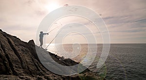 Silhouette of young man fishing on the rocks holding fishing rod with lens flare in phuket Thailand
