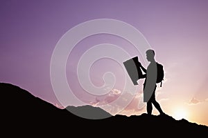 Silhouette of young man looking at a map in nature while hiking