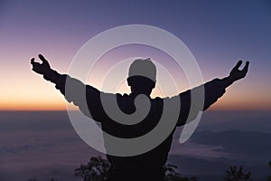 Silhouette of a young man praying to God on the mountain at sunset background.  raising his hands in worship. Christian Religion