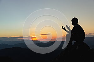 Silhouette of a young man praying to God on the mountain at sunset background. Woman raising his hands in worship. Christian