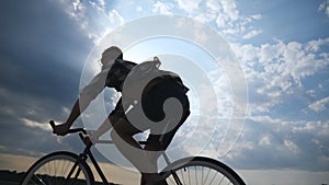 Silhouette of young man riding at vintage bicycle with beautiful sunset sky at background . Sporty guy cycling in the