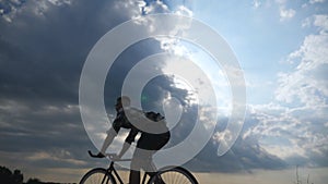 Silhouette of young man riding at vintage bicycle with beautiful sunset sky at background . Sporty guy cycling in the